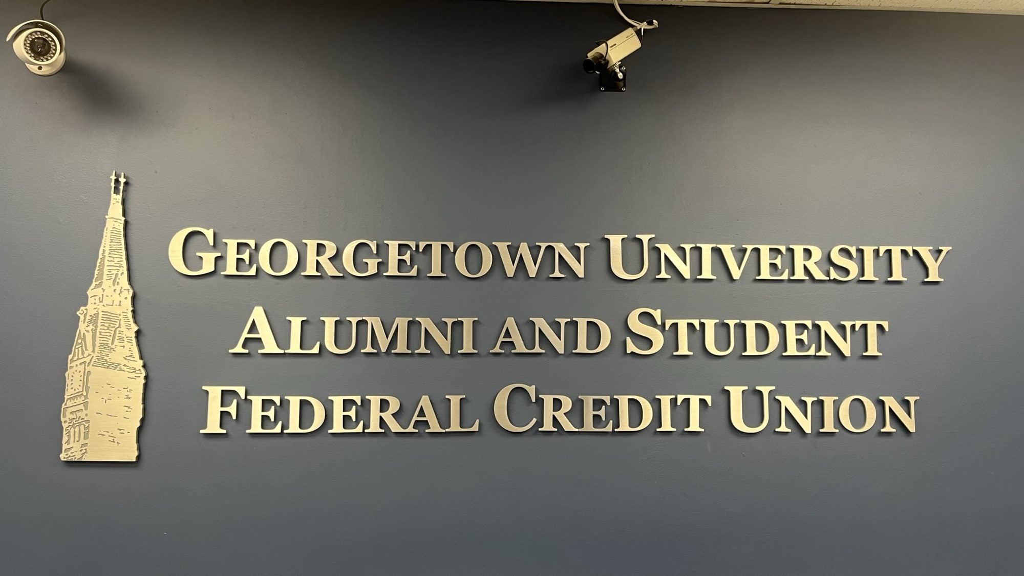 A wall with gold lettering introducing the Georgetown University Alumni and Student Federal Credit Union, with a gold Healy Tower next to it