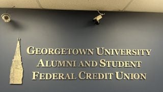 A wall with gold lettering introducing the Georgetown University Alumni and Student Federal Credit Union, with a gold Healy Tower next to it