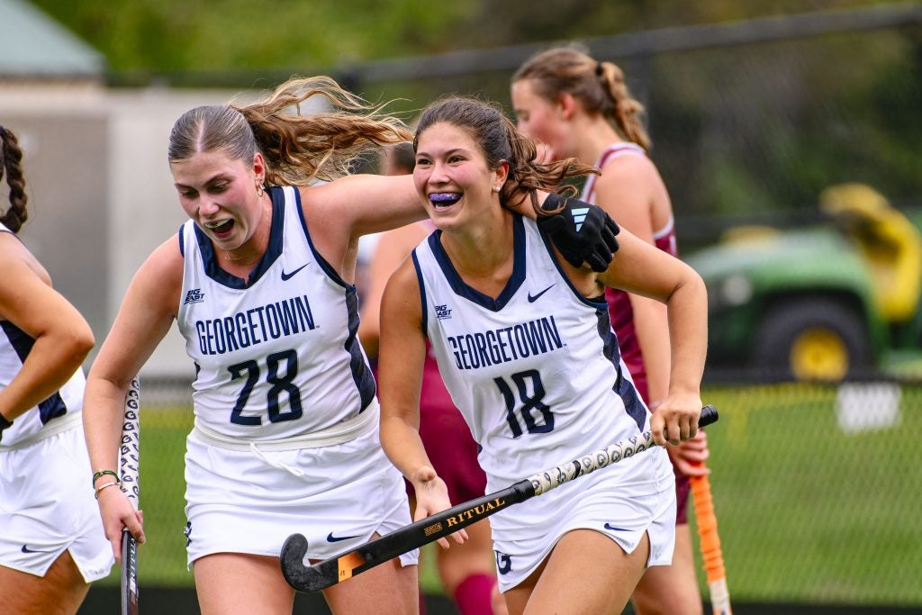 Two female field hockey players in white jerseys celebrate a point.