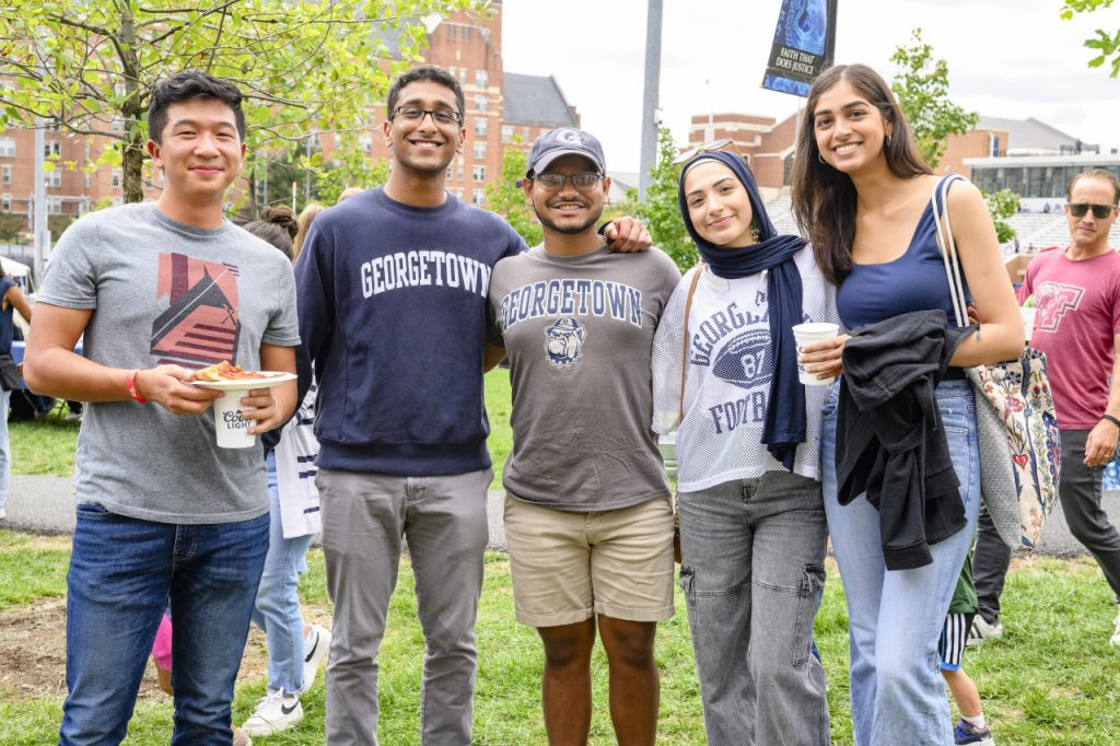 A group of alumni wearing Georgetown T-shirts and sweatshirts pose and smile for a picture during Homecoming Weekend. 