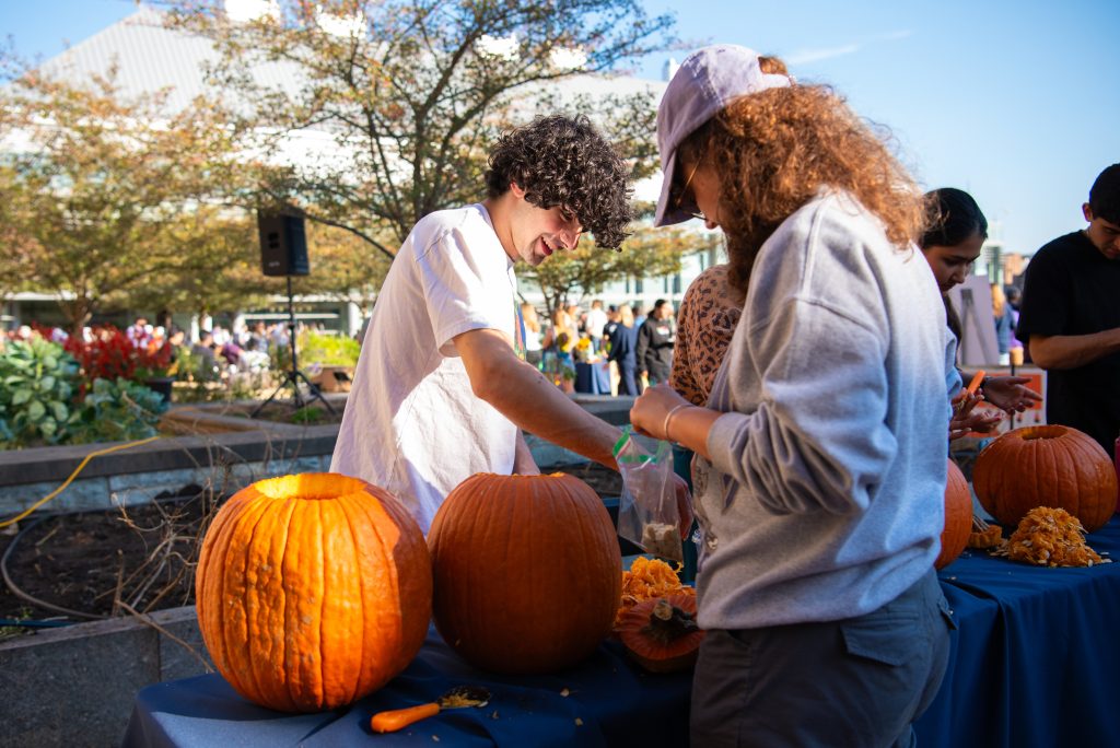 Two students carve pumpkins outside on a sunny day.