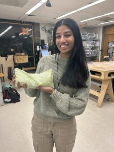 Student smiles at the camera holding their creation from the makerhub, a heating pad