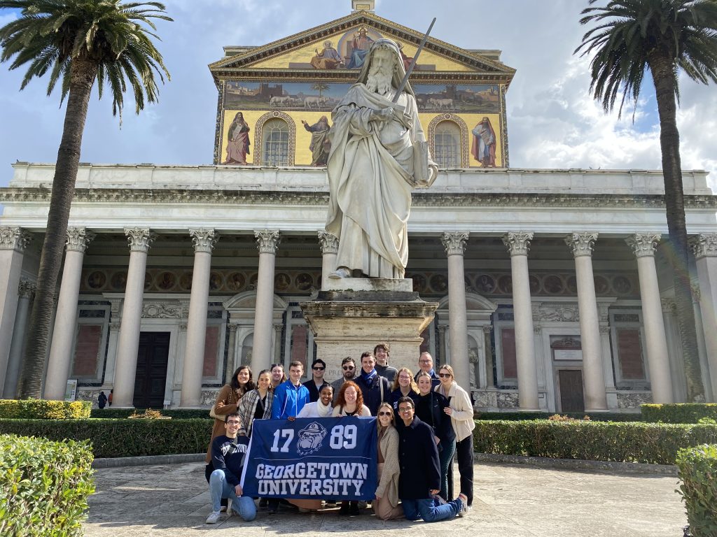 Students standing in Rome while holding a Georgetown flag