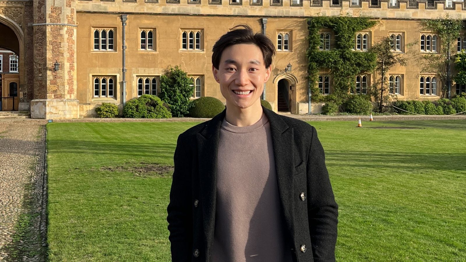 Charlie Wang in a jacket standing on a green lawn