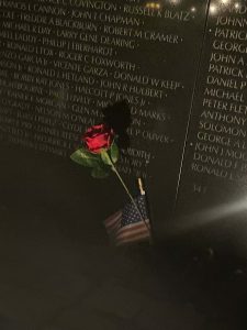 A single red rose with a miniature American flag lay against the list of names inscribed in the memorial