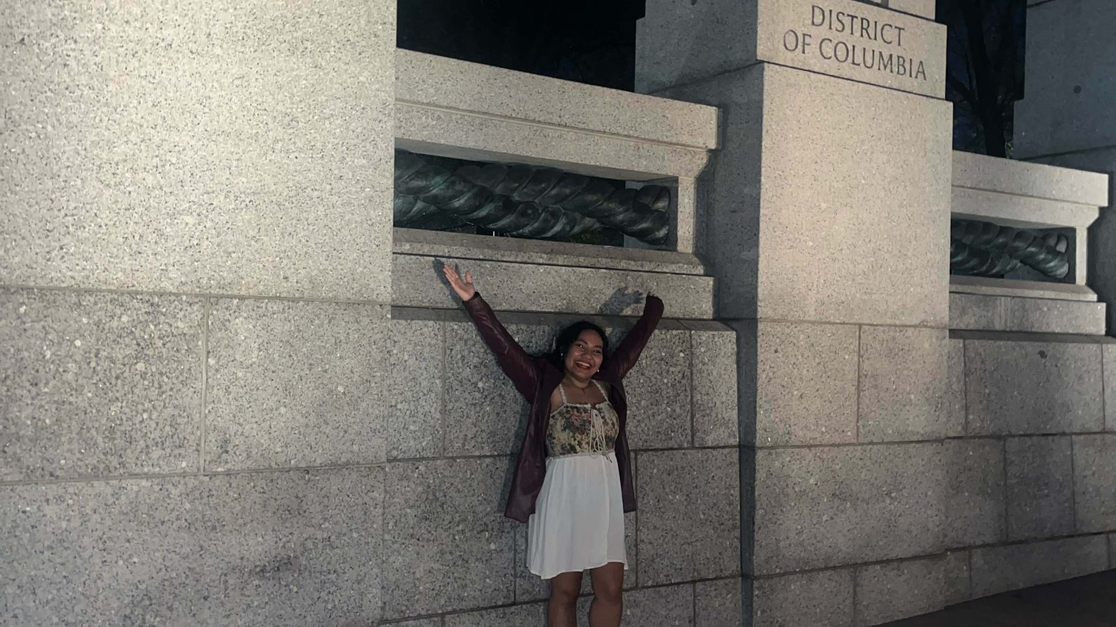 Mara stands with her arms wide between the Hawaii and DC monuments at the World War 2 Memorial