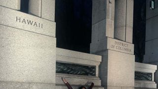 Mara stands with her arms wide between the Hawaii and DC monuments at the World War 2 Memorial