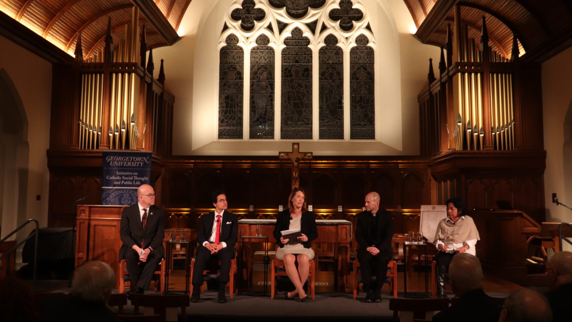 A panel of four people speak in a dimly lit chapel