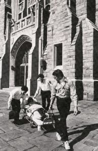 A black-and-white photo of student medical volunteers transporting a student on a stretcher on Georgetown's campus in 1984.