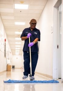 A custodian mops the floor of a well-lit corridor.