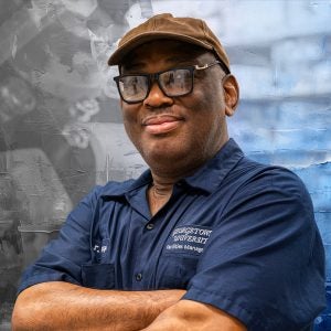 A graphical treatment of a custodian posing with his arms crossed and smiling slightly at the camera. He wears a navy uniform, a tan baseball cap and black glasses.