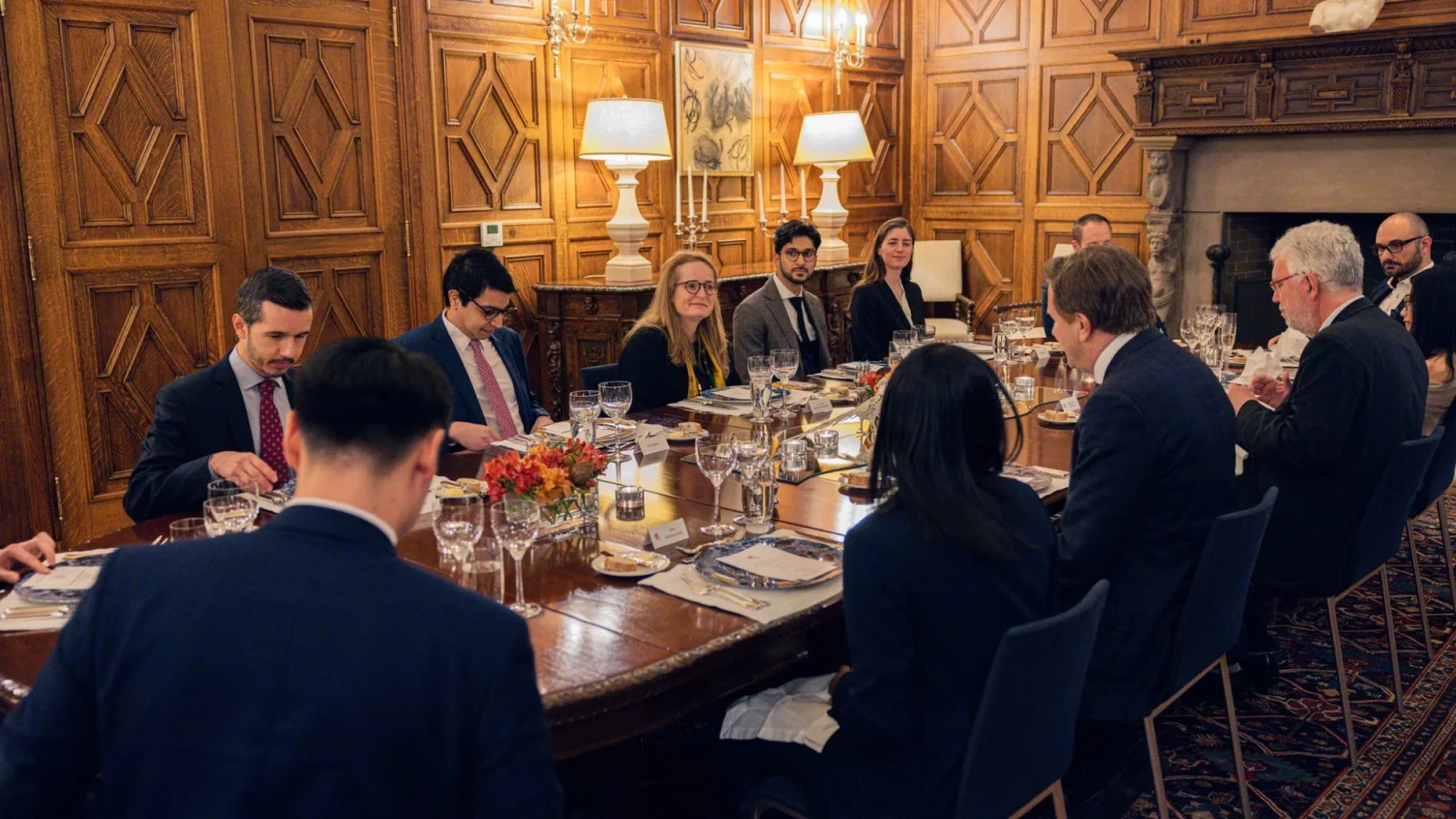 A group of graduate students dressed in suits sit around a dining room table in an elegant room.