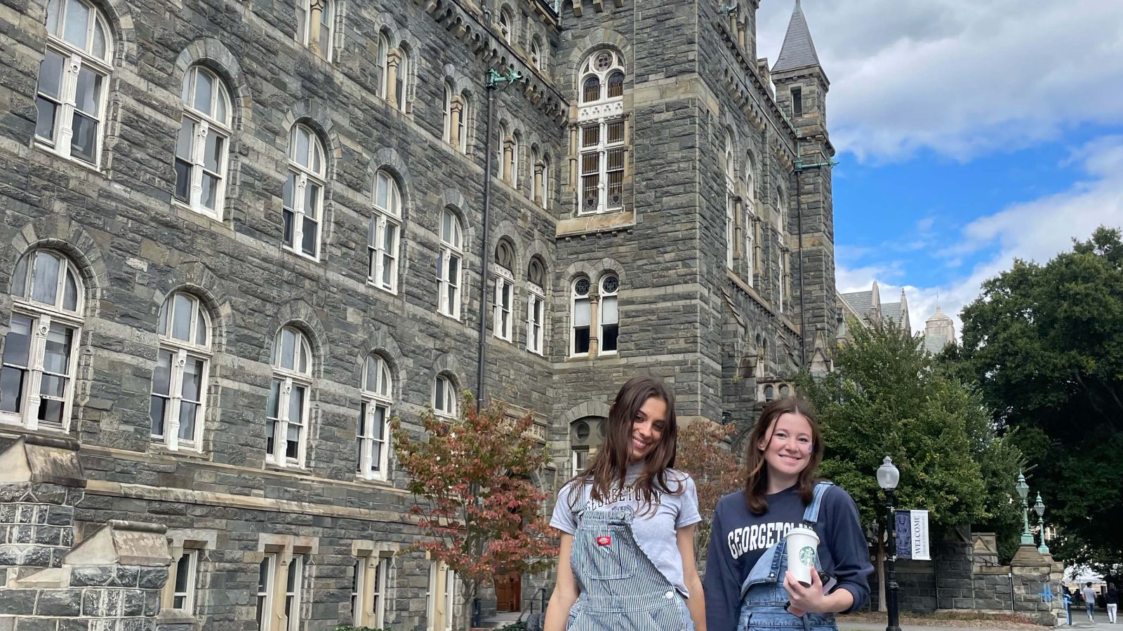 Ava and a friend stroll hand in hand in front of Healy hall while in Georgetown attire