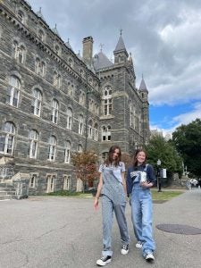 Ava and a friend stroll hand in hand in front of Healy hall while in Georgetown attire