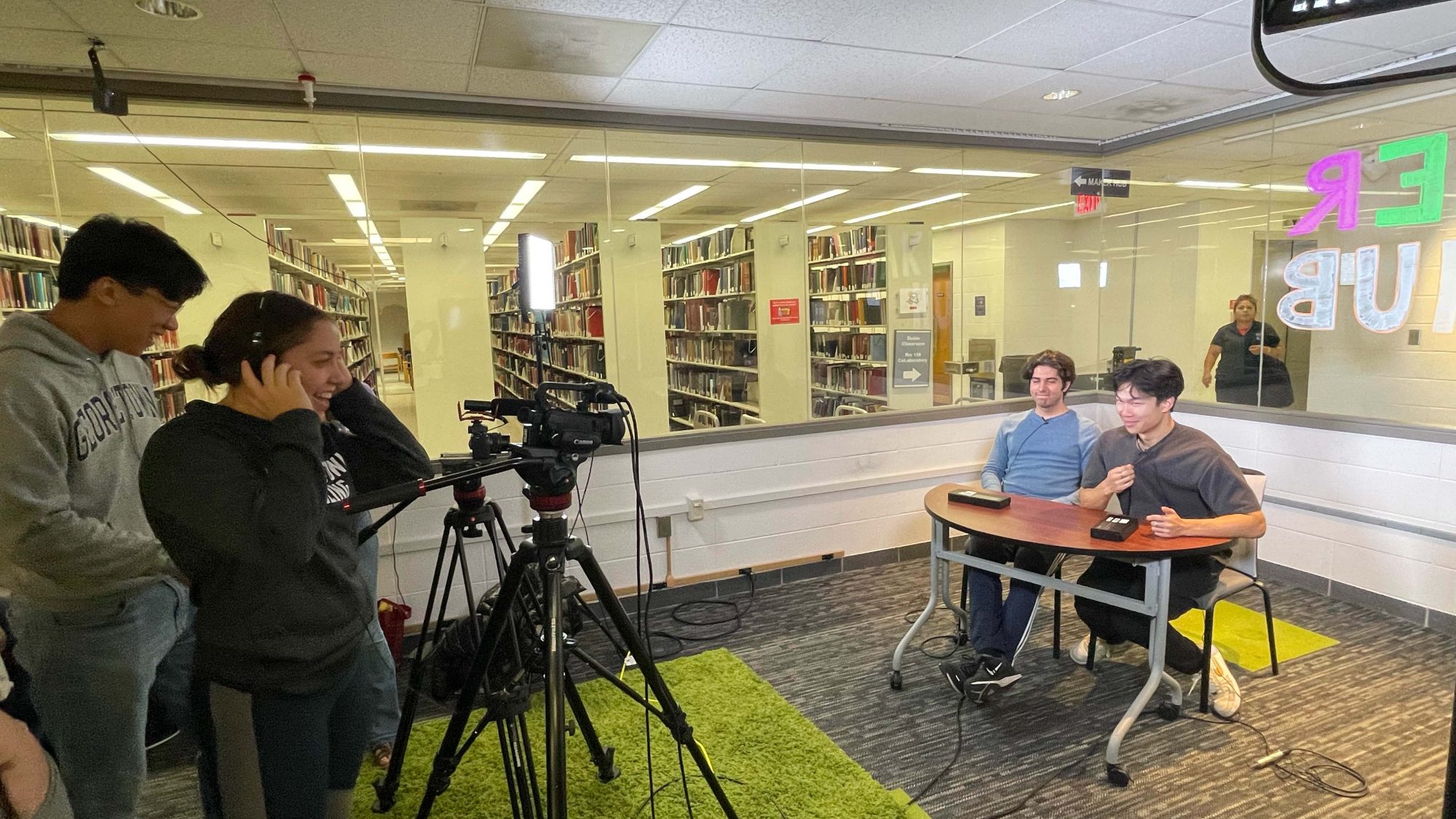 Students practice podcasting, with two students operating cameras and lighting, and another two students being filmed at a desk