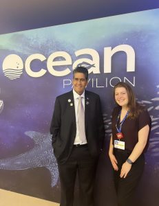 A young woman stands next to a man in a suit in front of a sign that says "Ocean Pavilion"