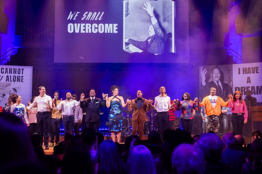 A group of performers hold hands onstage and are about to take a bow to close out their performance at the Kennedy Center.