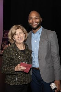 The female board chair of a theater company stands with the company's artistic director. 