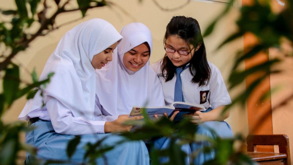 Three school girls reading together in Indonesia.