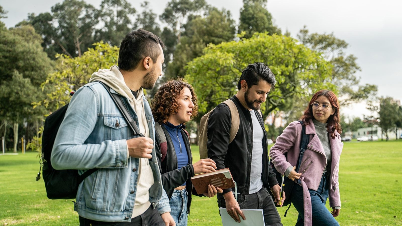 Four Latino college students walk and talk to each other on a college campus
