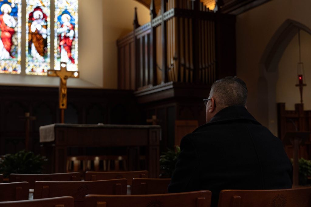 Man sits in a chapel while staring at the altar.