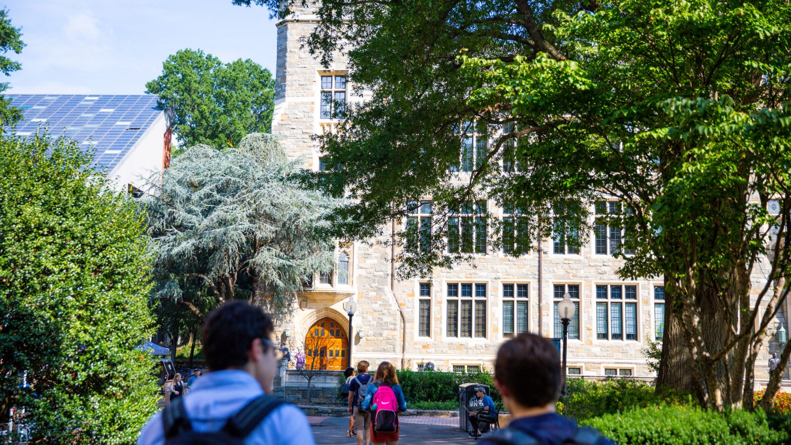Students on a summer day walk toward a stone building on Georgetown&#039;s campus.