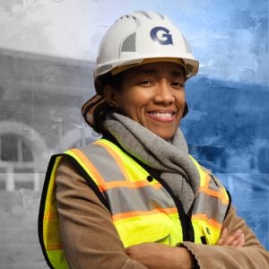 A Black woman wearing a yellow vest smiles while wearing a hard hat with a "G" on the front for Georgetown.