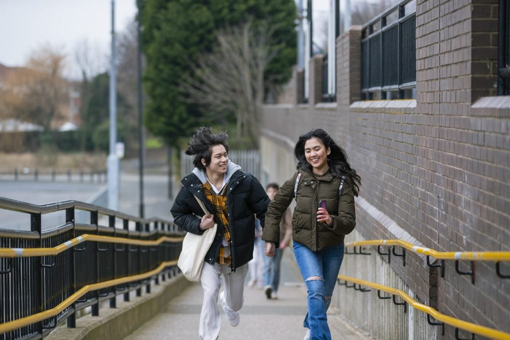 A close-up front-view shot of a teenage couple running up a concrete ramp while holding hands in Wallsend, North East England. They are trying to catch the next train on the Subway.