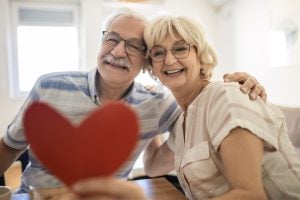 Smiling senior woman receives present box and kissing her husband at home