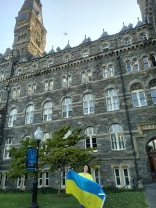 Ksenia Dubova holding a Ukrainian flag in front of Healy Hall