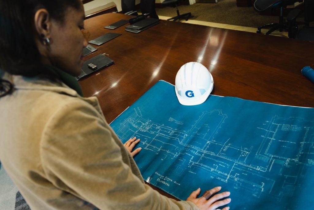 A woman looks down at plans for a building in the early 20th century. 