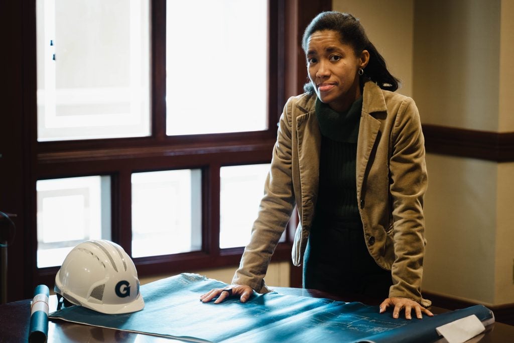 A Black female architect stands with her hands on plans in front of a window.