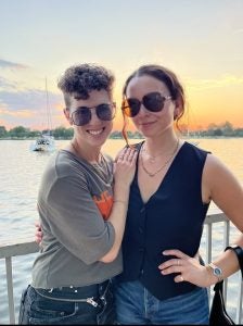 A couple pose in front of a sunset over the water.