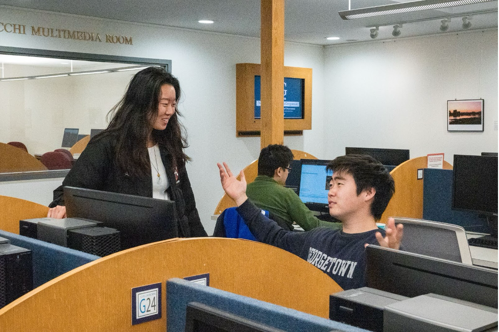 Two students have a conversation at the computer lab in the multimedia room