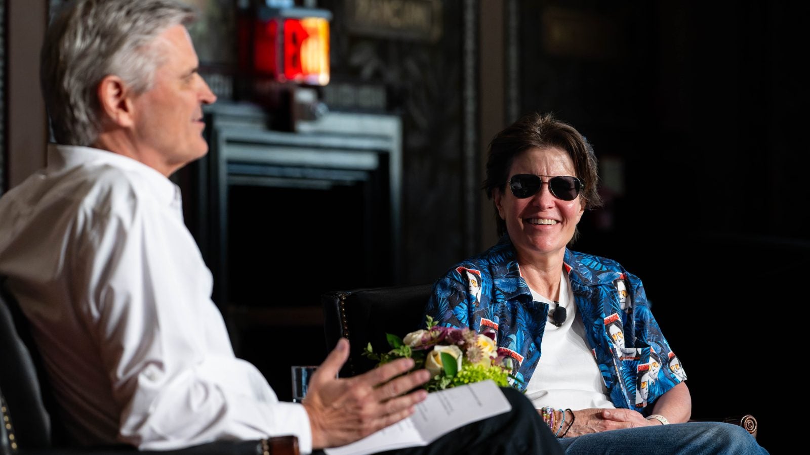 Kara Swisher, a tech podcast host and journalist, smiles on stage wearing aviator sunglasses and a blue shirt.