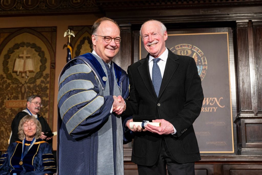 Georgetown's president (left) stands with a professor accepting an award onstage of an event venue at Georgetown.