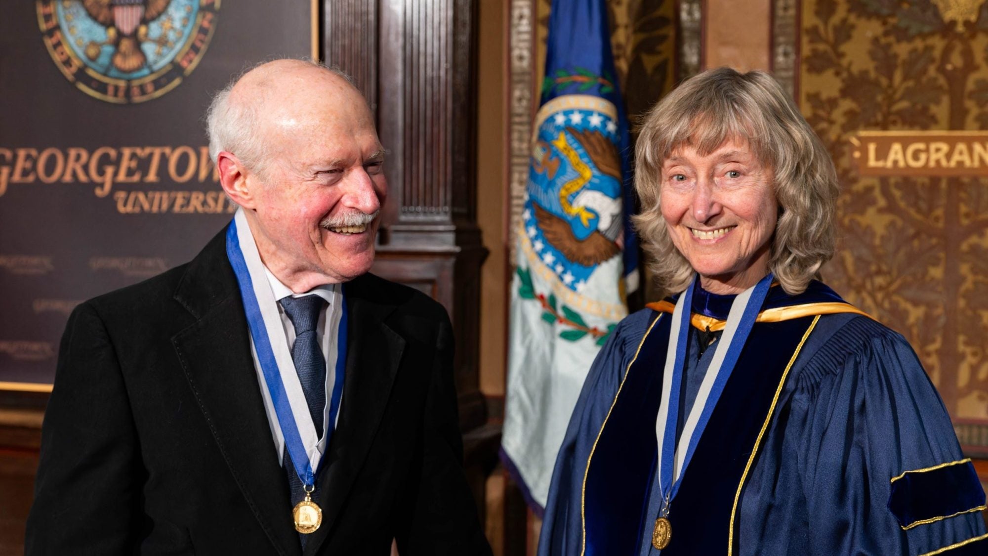 A husband smiles at his wife on stage after they both participated and were honored in Georgetown's spring faculty convocation.