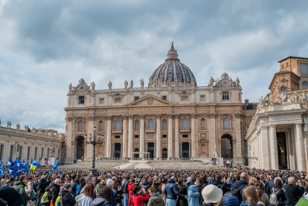 A huge group of people gather outside  St. Peter’s Basilica at Vatican City on a cloudy day