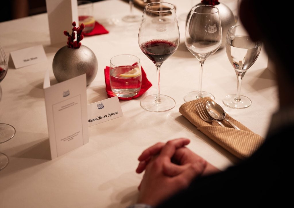 A man with folded hands at a formal dinner setting.