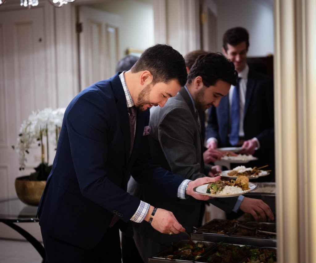 A man in a suit is grabbing food from a buffet table