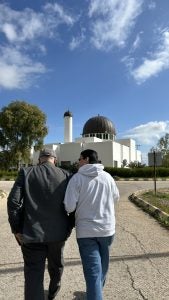 An older and younger man walk together toward al-Bayt University. 