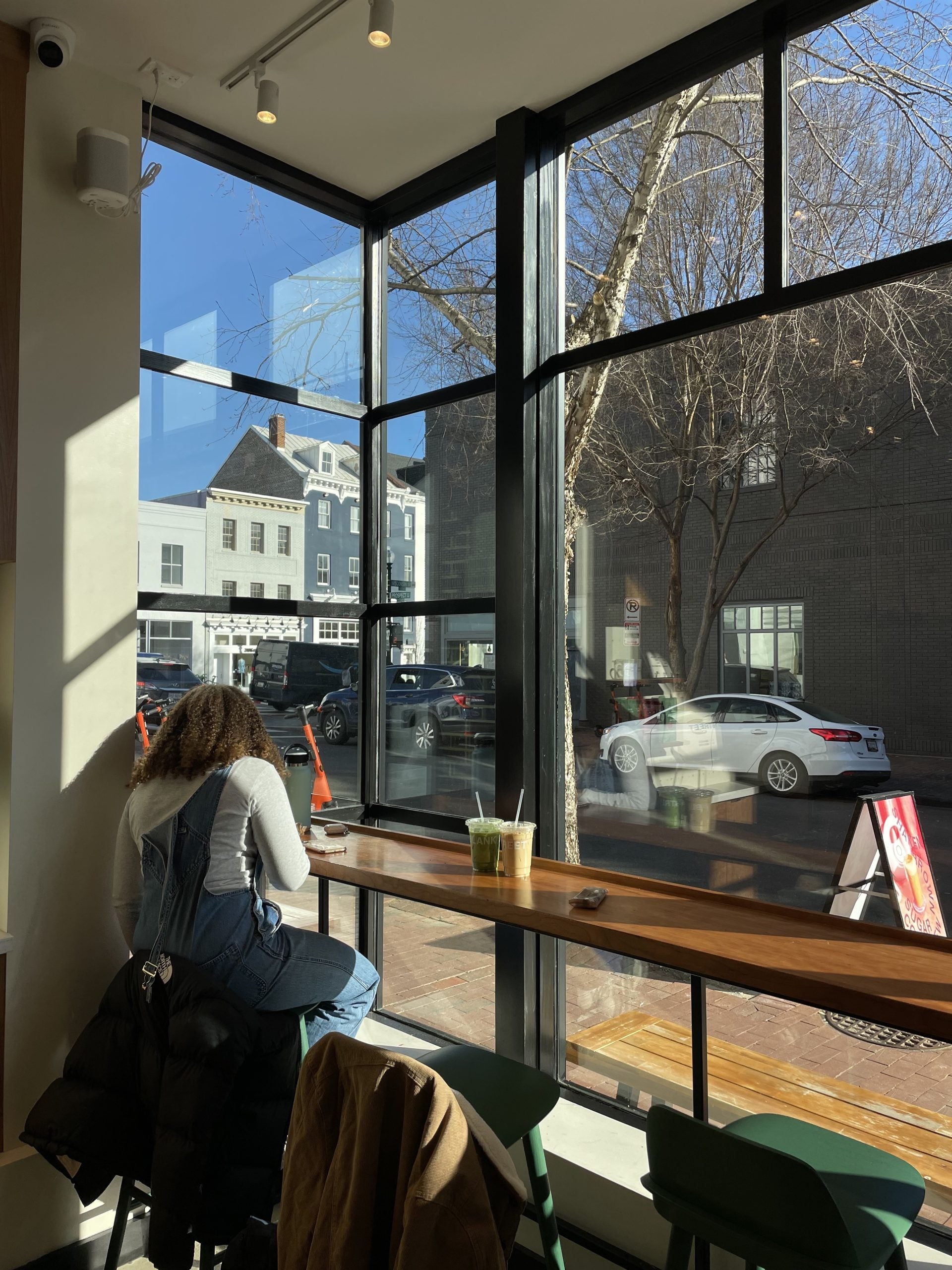 A girl sits at the window of a coffee shop, over looking Prospect Street and Wisconsin Avenue