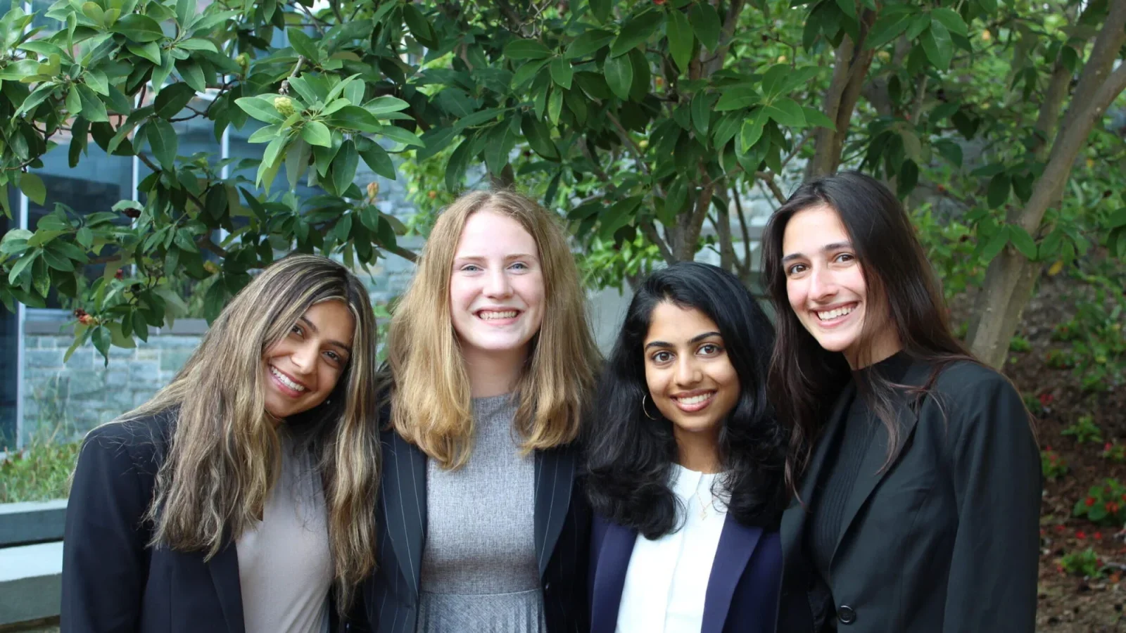 A group of women pose and smile together under a tree.