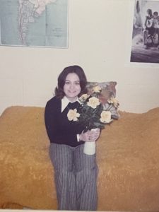 A young woman holding photos while sitting in a dorm room.