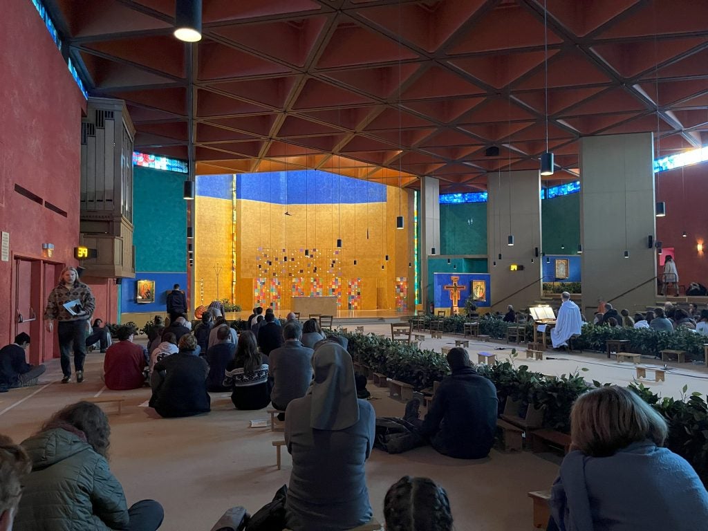 Interior of a church with dozens of people kneeling or sitting on the floor facing the front of the church.