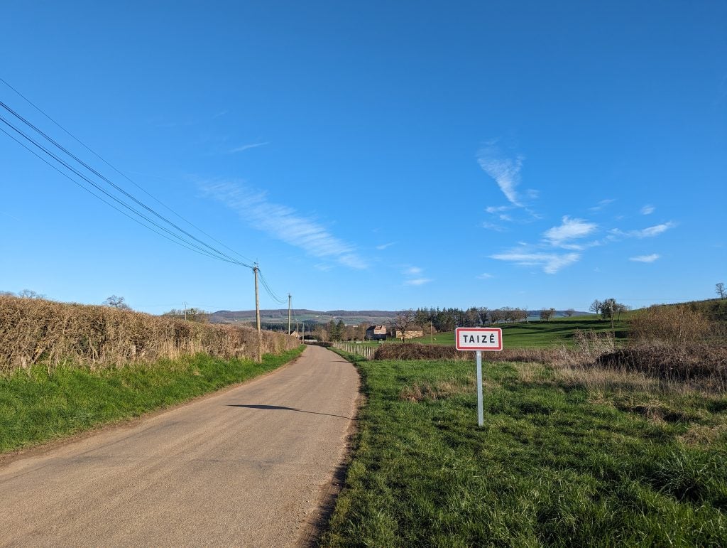 A dirt road in a field with a road sign reading Taize on a sunny clear day.