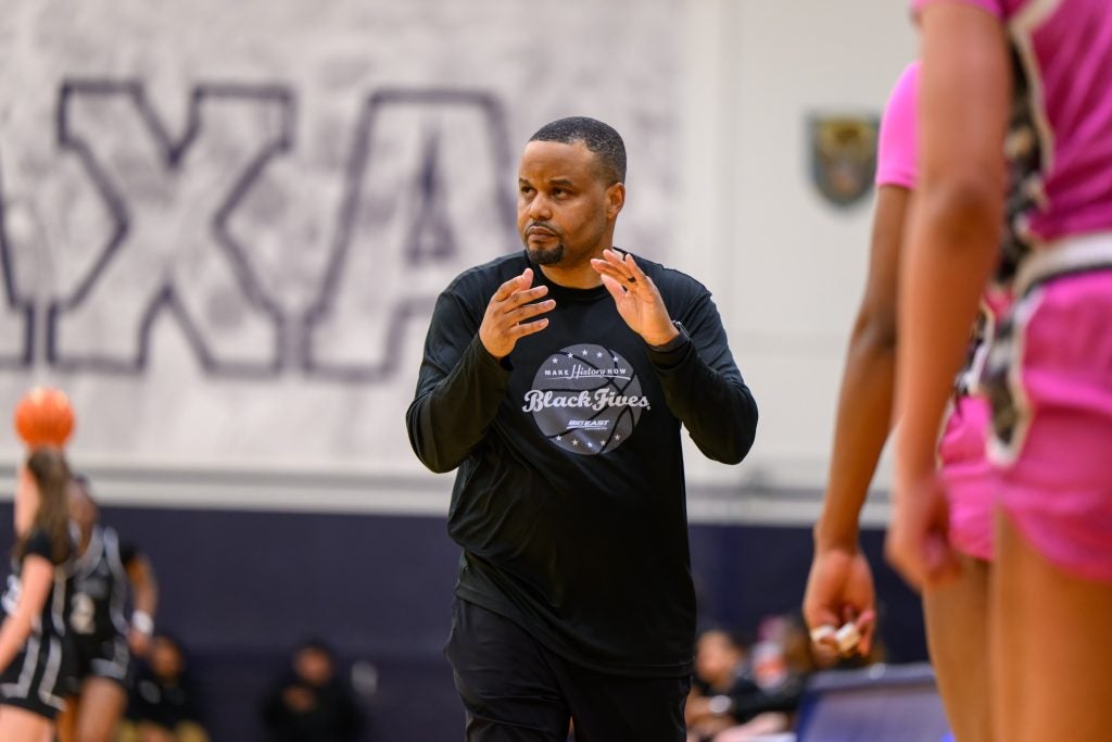 Head Women's Basketball Coach Darnell Haney walks down the sideline during a game clapping his hands.
