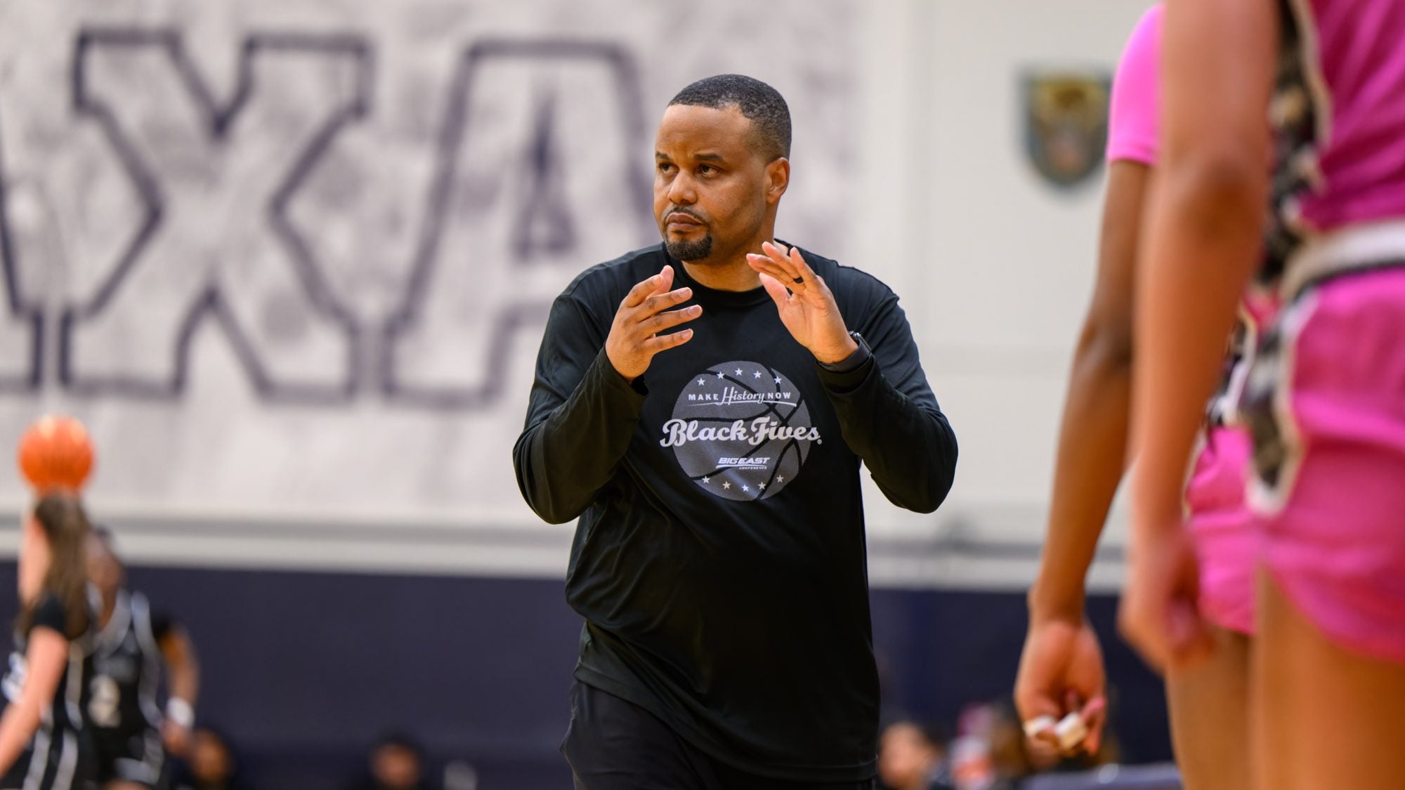 Head Women's Basketball Coach Darnell Haney walks down the sideline during a game clapping his hands.