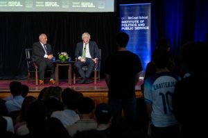 Two men sit on stage discussing politics in front of a crowd of students.