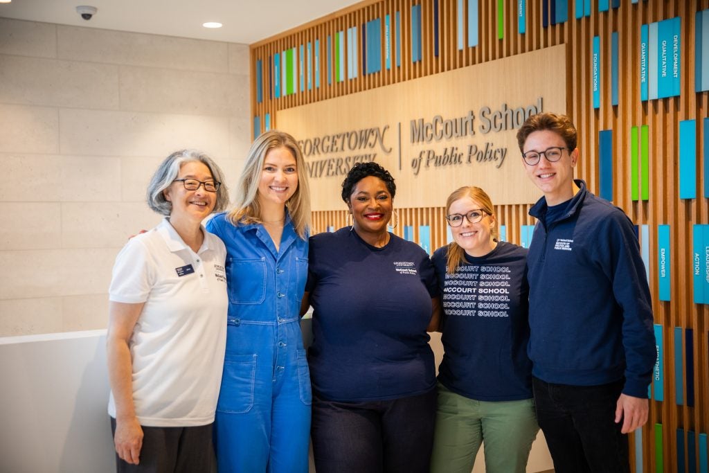 A group of students and staff stand in front of a sign that says "McCourt School of Public Policy."